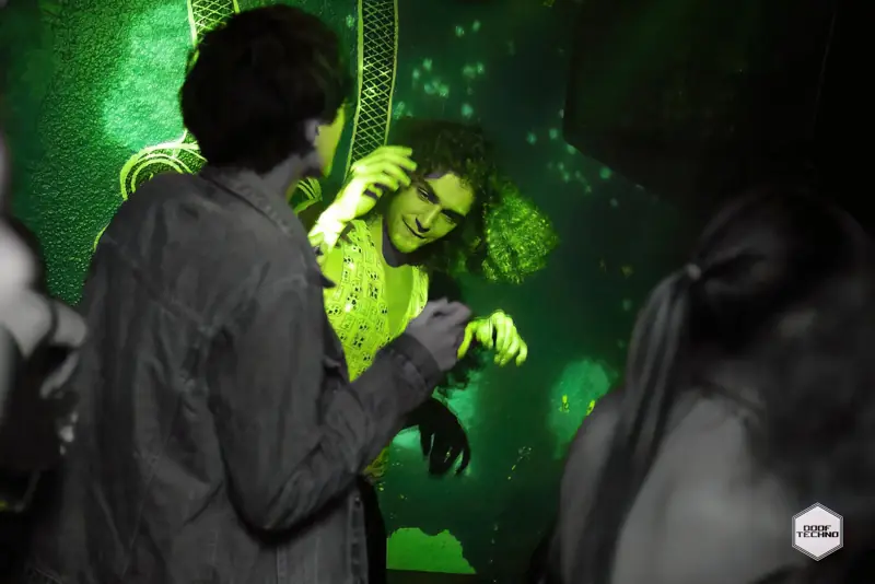 A dancer lit bright green throws shapes beside the mural. Launch night, May 2025
