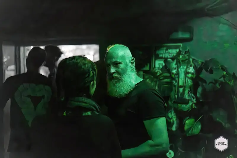 A bearded regular deep in conversation on the floor. Launch night, May 2025