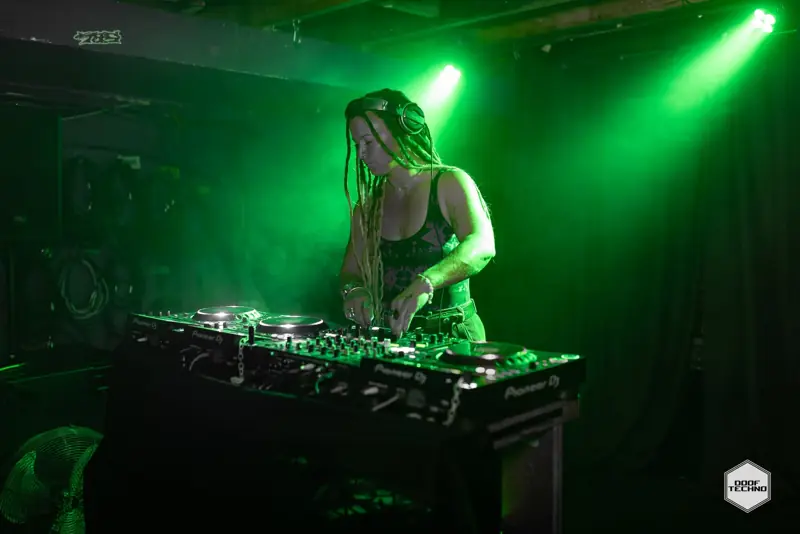 A DJ with long braids plays under the green spots
