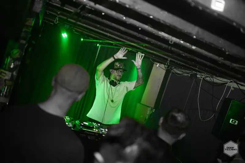 A DJ with both hands up in the booth